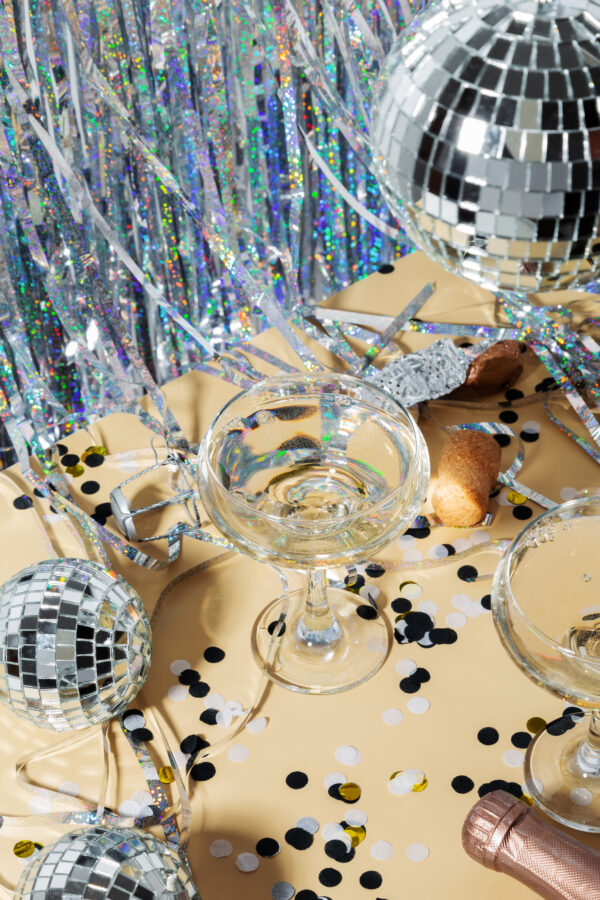Happy new year celebration concept theme with close up on two glasses of champagne with shiny silver disco ball and confetti. Trendy party time symbols concept